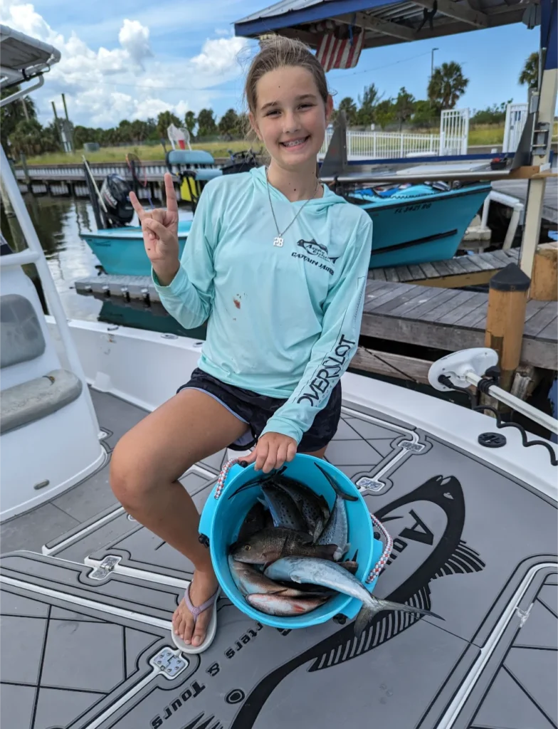 Young angler on the bow holding a bucket of her catch