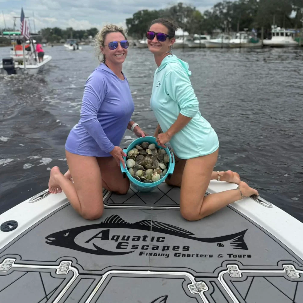 Two guests holding a bucket of bay scallops on the bow of the Aquatic Escapes boat