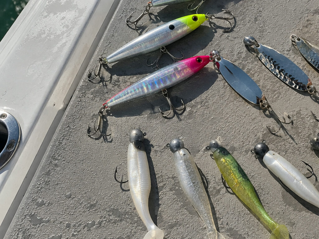 Casting plugs, silver spoons and jig heads with paddle tail soft plastics laid out on the deck of the boat