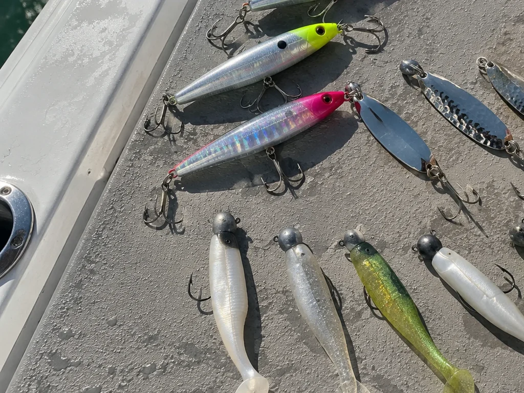Casting plugs, silver spoons and jig heads with paddle tail soft plastics laid out on the deck of the boat
