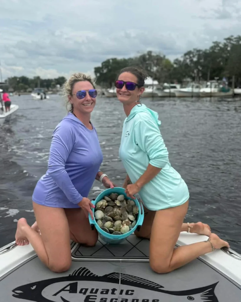 Two guests kneeling with a bucket of bay scallops on the bow of the Aquatic Escapes boat