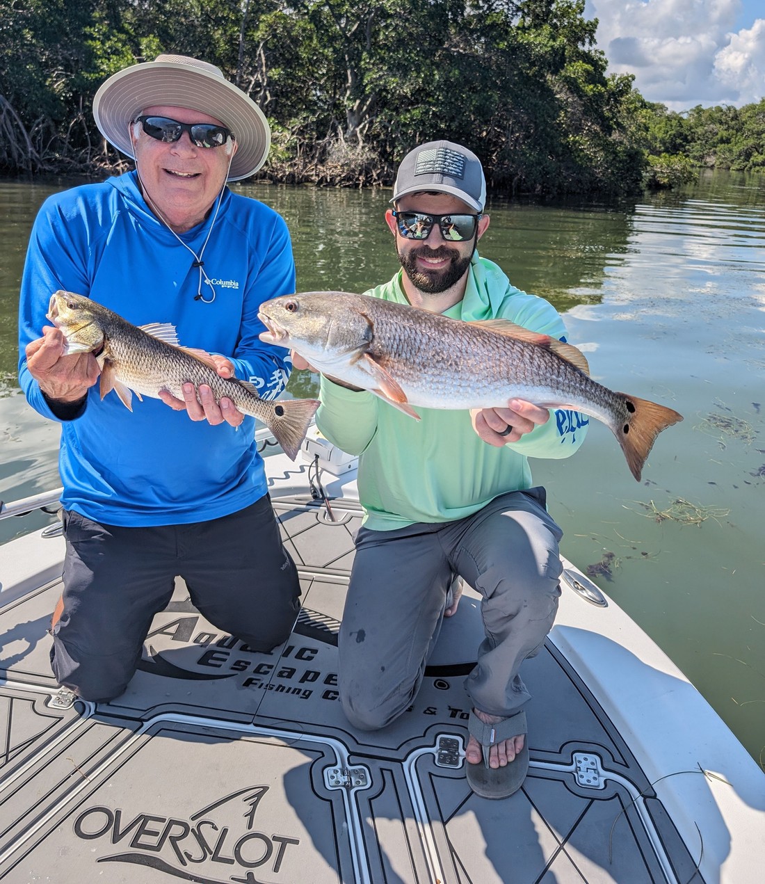 Two guests holding redfish on an Aquatic Escapes charter