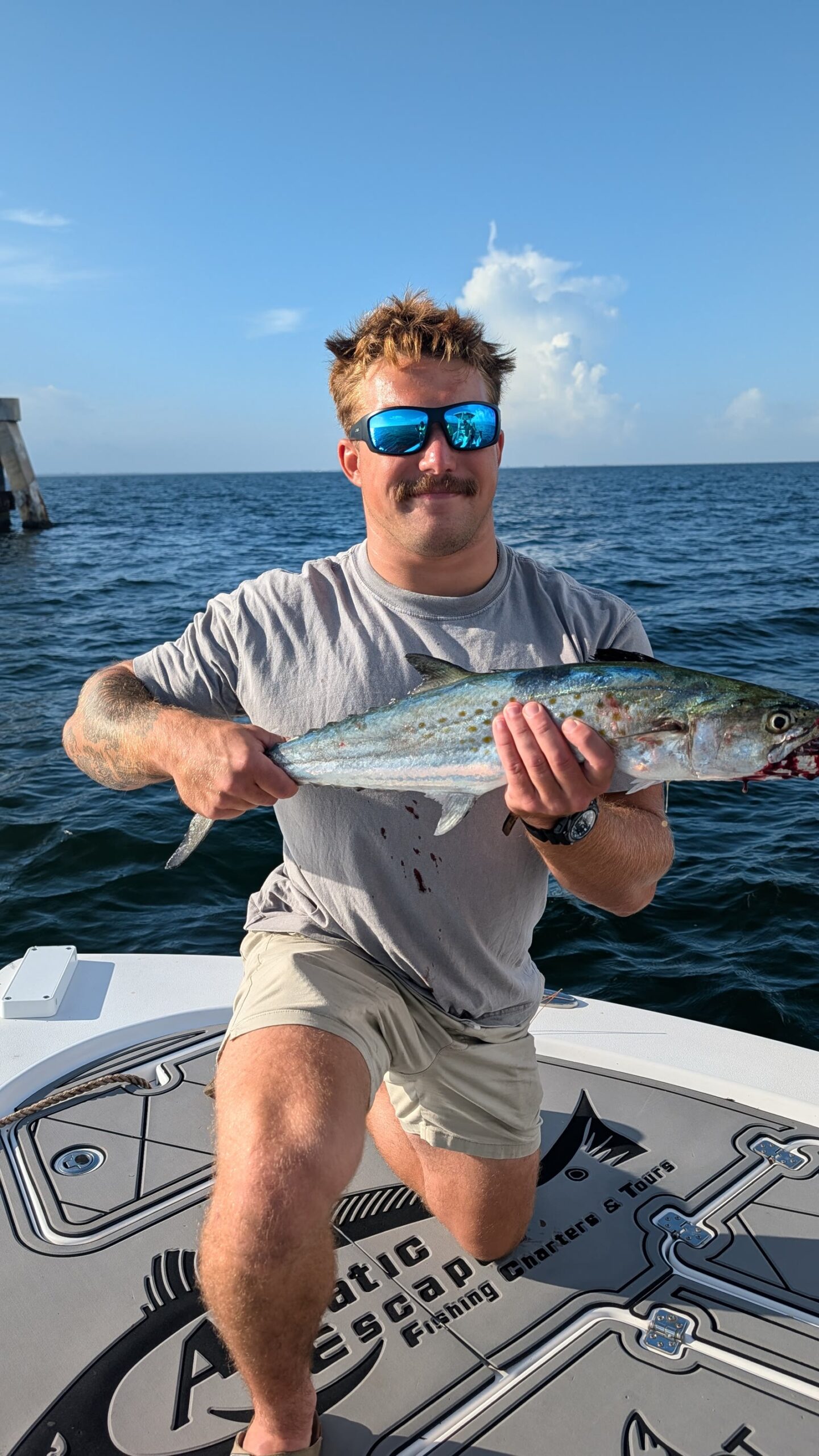 A guest holding a Spanish mackerel on the bow of the Aquatic Escapes boat with the Skyway behind