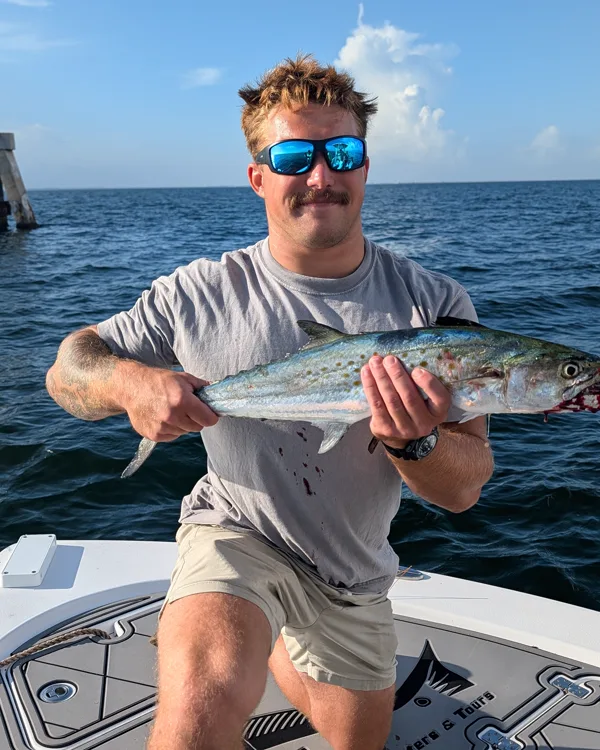 A guest holding a Spanish mackerel on the bow of the Aquatic Escapes boat